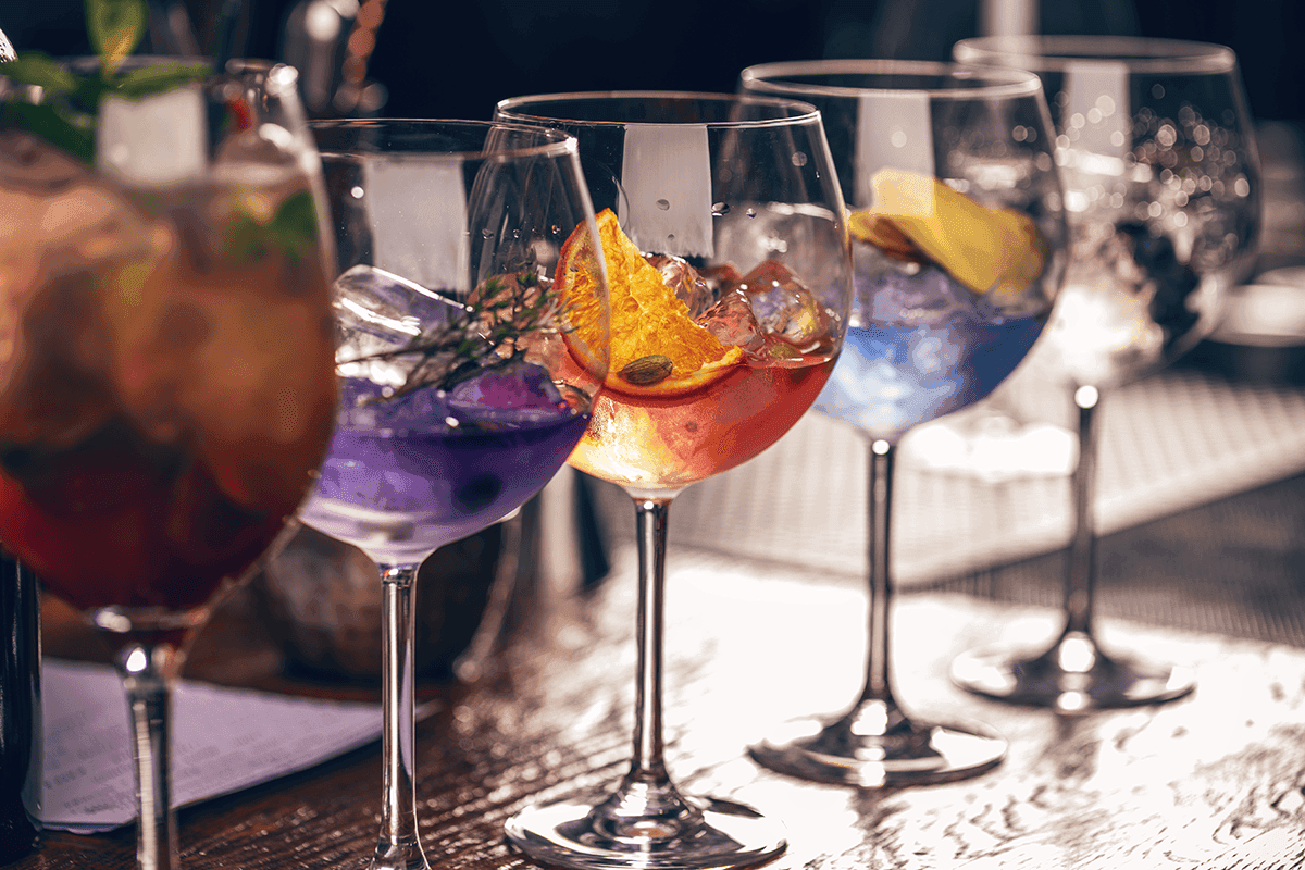 Row of garnished gin cocktails in balloon glasses along a bar, finished with dried citrus wheels and thyme